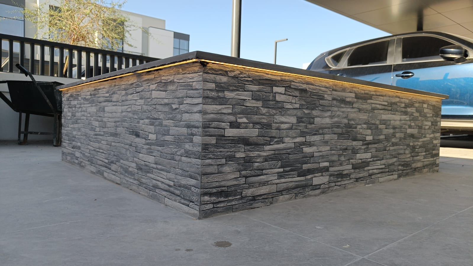 Corner detail of stone-clad planter with under-cap LED lighting on a light grey tiled patio
